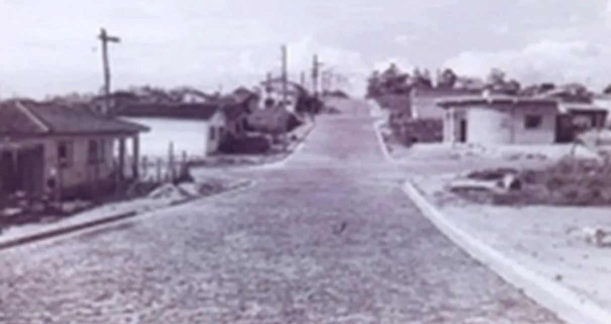 Foto antiga em preto e branco de uma rua de paralelepípedos com casas térreas e postes