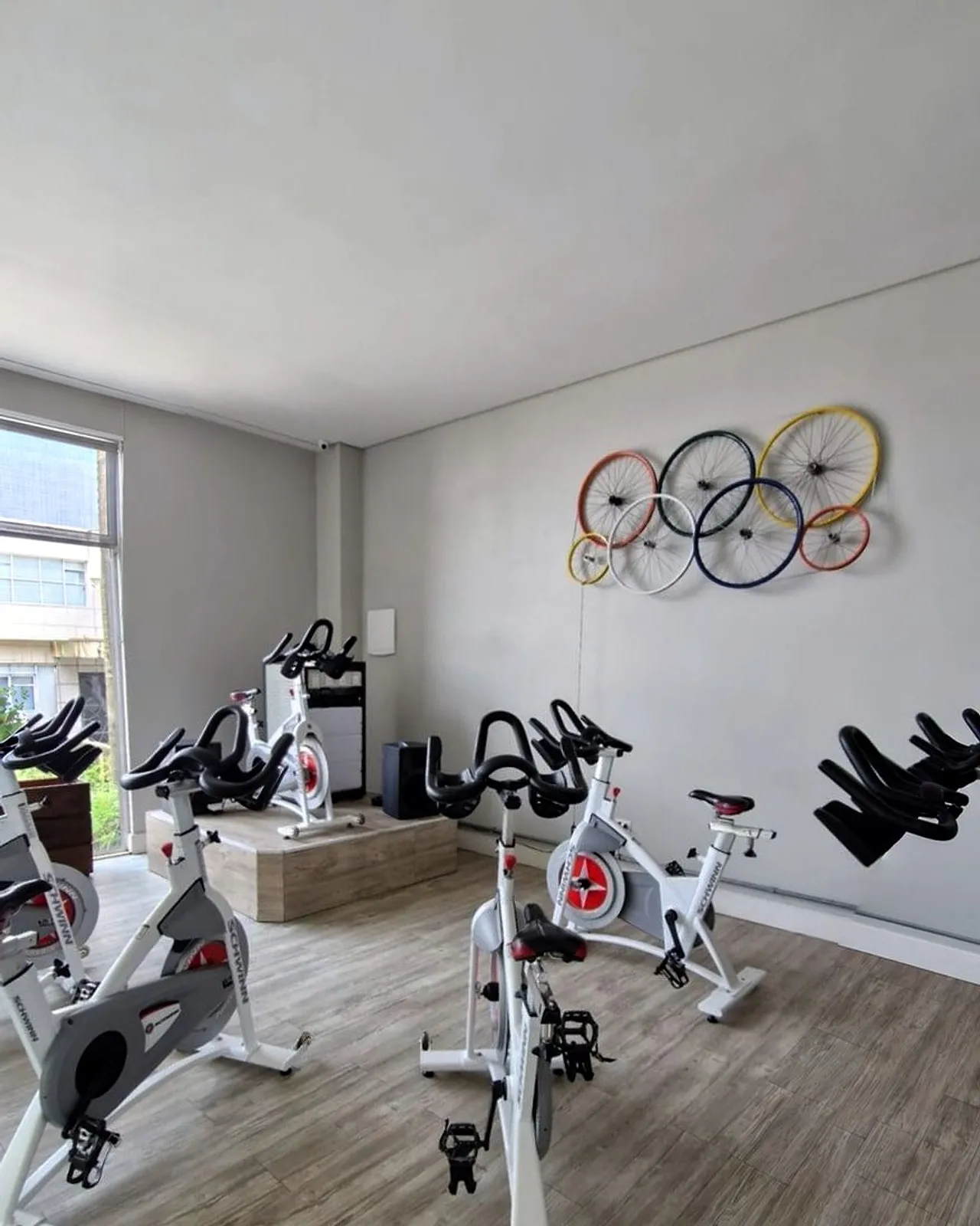 Sala de bike com bicicletas brancas, um tablado e rodas coloridas de bicicleta presas na parede