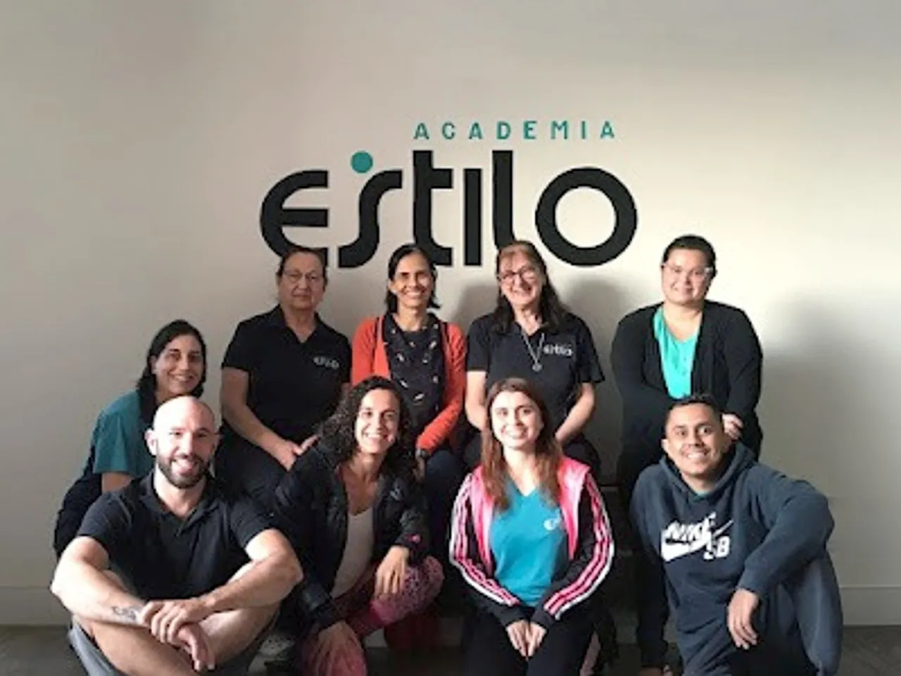 Equipe da Academia Estilo reunida diante do logotipo na parede