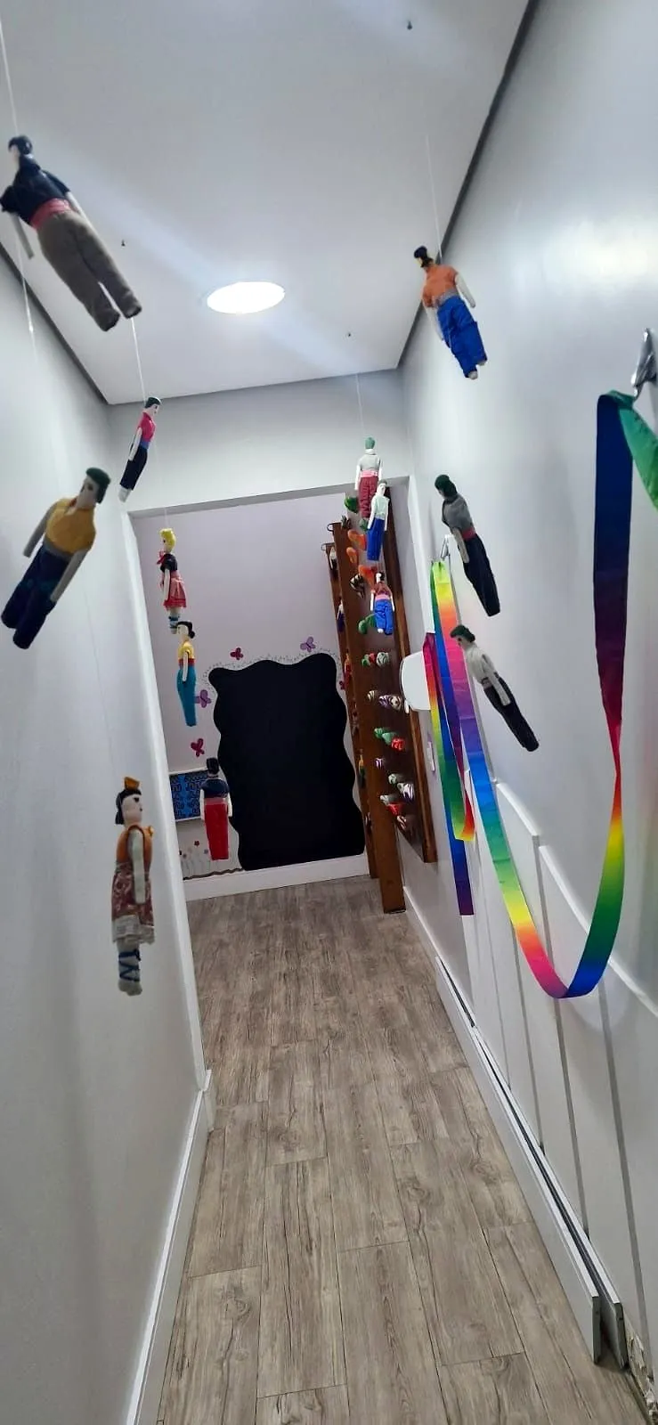 Corredor da sala de estimulação psicomotora com bonecos de pano pendurados, fitas coloridas e agarras na parede