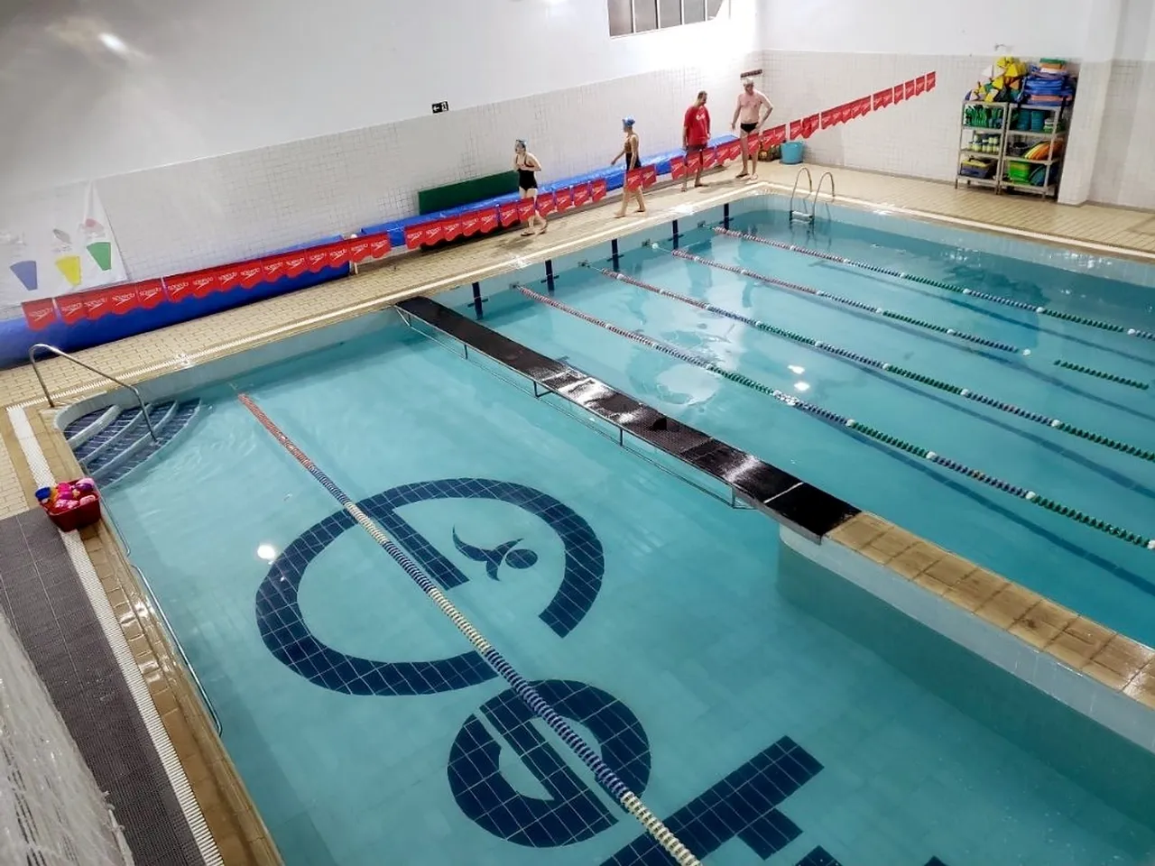 Piscina vista do alto, com uma plataforma atravessando a água e a marca da Estilo desenhada em azulejos no fundo